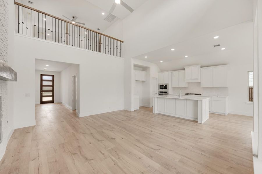 Open-concept living area with two-story ceiling, white kitchen island, and light hardwood floors