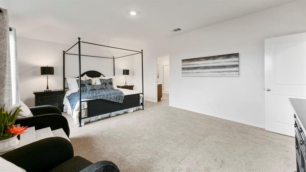 Carpeted bedroom with recessed lighting, an adjacent bathroom entry, a large window with patterned drapes, and a white paneled door Carpeted bedroom with recessed lighting, an adjacent bathroom entry, a large window with patterned drapes, and a white paneled door