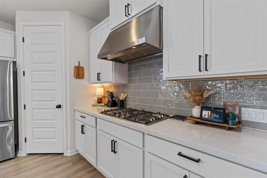 Kitchen with white cabinets, stainless steel appliances, light stone counters, decorative backsplash, and light wood finished floors