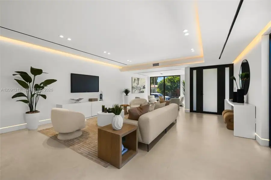 Modern living space featuring recessed ceiling lighting, cove LED accent lighting, smooth neutral-toned flooring, and a glass-paneled entry door with black frame Modern living space featuring recessed ceiling lighting, cove LED accent lighting, smooth neutral-toned flooring, and a glass-paneled entry door with black frame