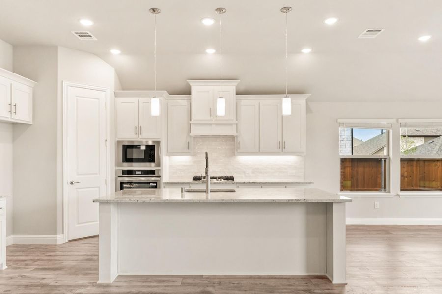 Kitchen with white cabinets, granite island, stainless steel appliances, and pendant lights over large center island Kitchen with white cabinets, granite island, stainless steel appliances, and pendant lights over large center island