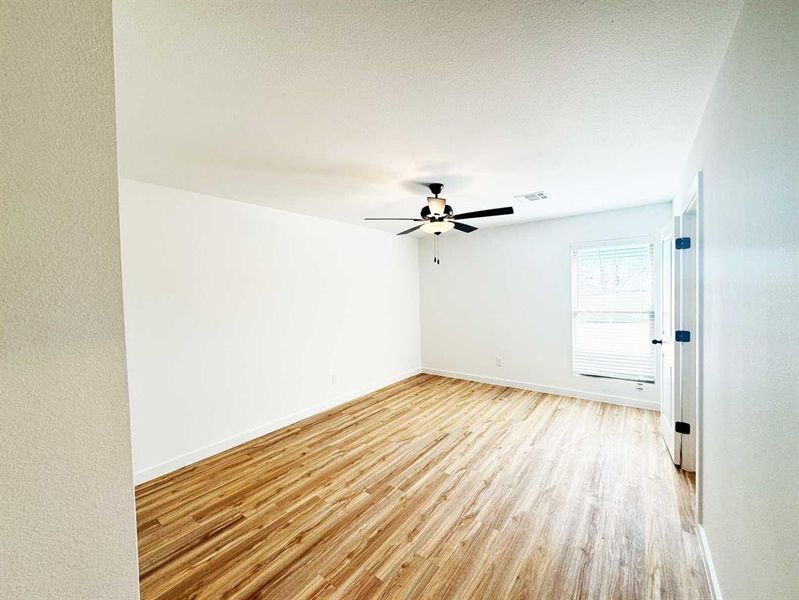 Empty room with baseboards, a ceiling fan, visible vents, and light wood-type flooring