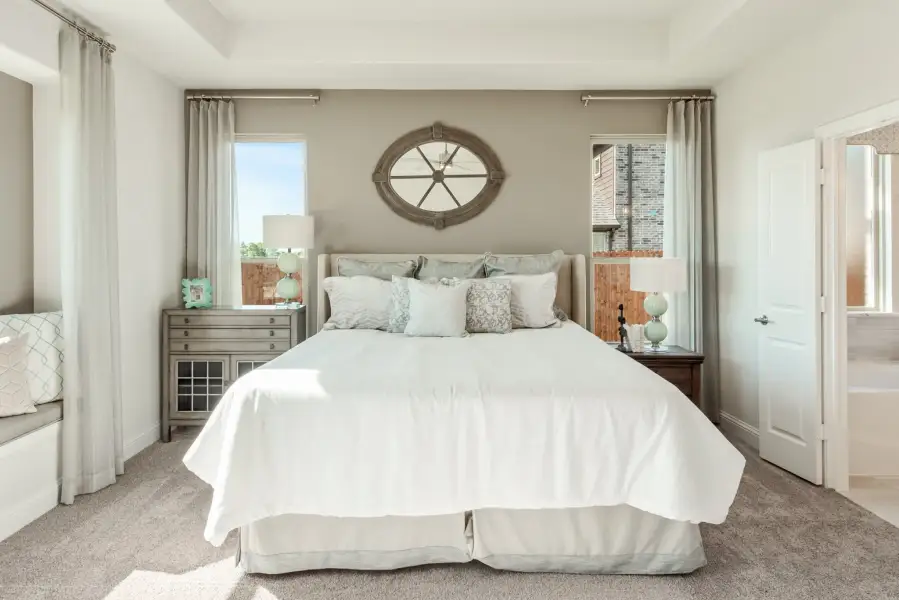 Master bedroom with king bed, neutral carpet, two windows, and decorative oval mirror above headboard