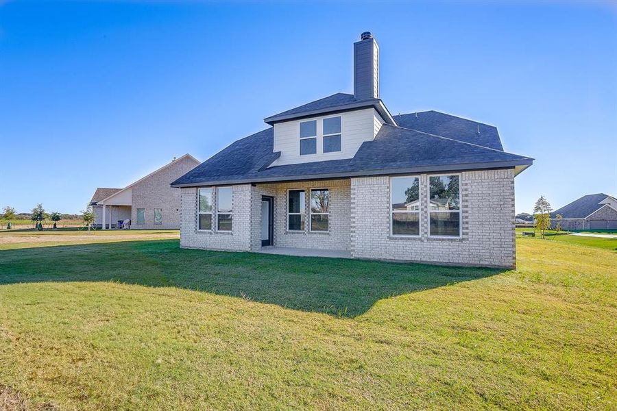 Rear view of house with brick siding, a yard, a patio, and a chimney