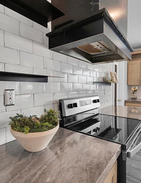 Kitchen featuring wall chimney exhaust hood, stainless steel electric range, tasteful backsplash, open shelves, and dark stone counters Kitchen featuring wall chimney exhaust hood, stainless steel electric range, tasteful backsplash, open shelves, and dark stone counters
