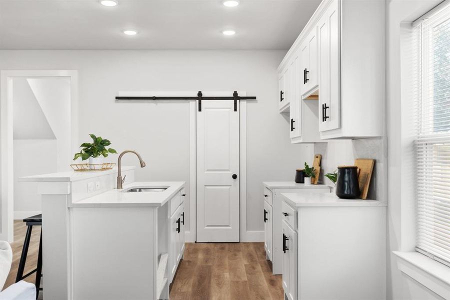 Kitchen with a barn door, white cabinets, a kitchen breakfast bar, light wood-type flooring, and a sink