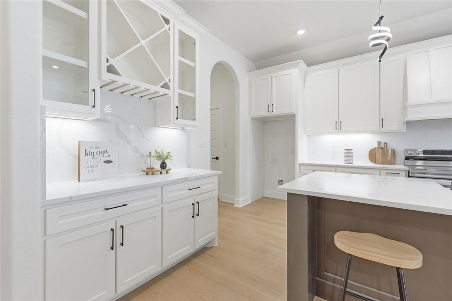 Kitchen with white cabinets, glass insert cabinets, arched walkways, and stainless steel electric stove