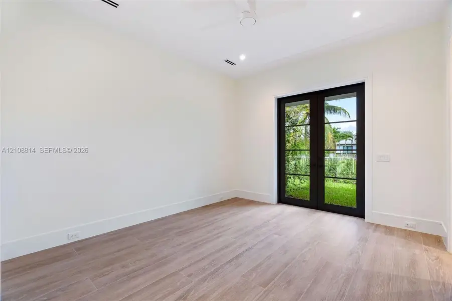 Neutral interior featuring porcelain-finish flooring, recessed lighting, a ceiling fan, and French doors with black frames opening to exterior landscaping Neutral interior featuring porcelain-finish flooring, recessed lighting, a ceiling fan, and French doors with black frames opening to exterior landscaping