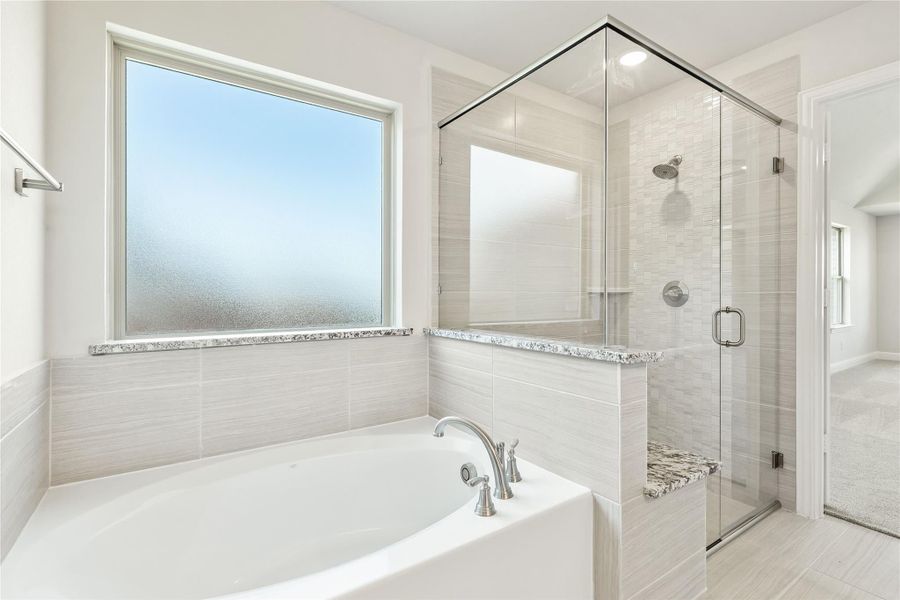 Master bathroom with soaking tub, glass-enclosed shower, and light gray tile walls