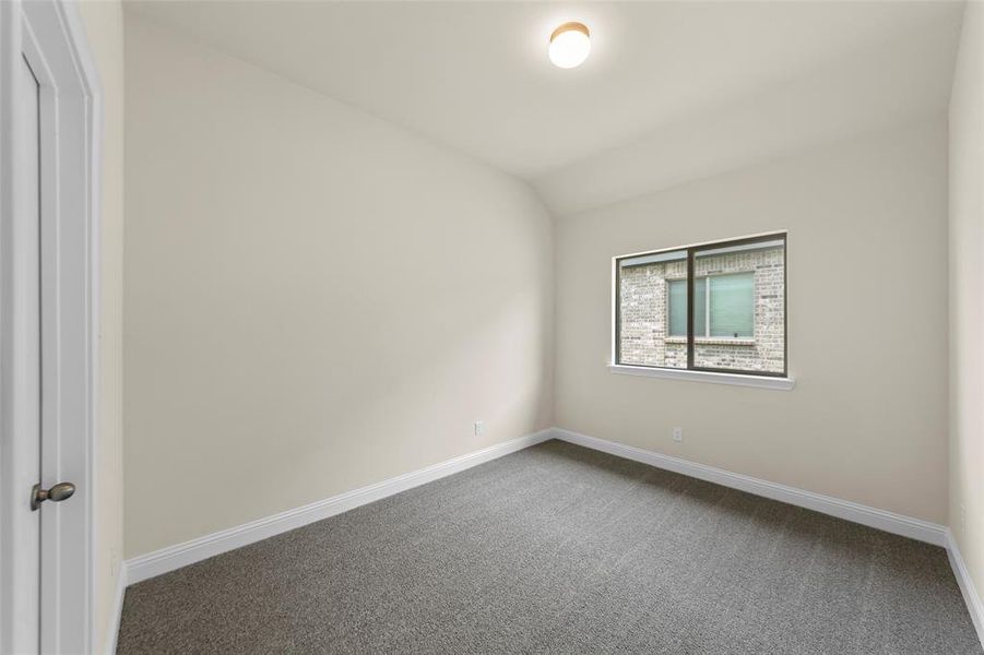 Bedroom featuring neutral wall color, gray carpeting, white baseboards, and a window with a view of exterior brickwork