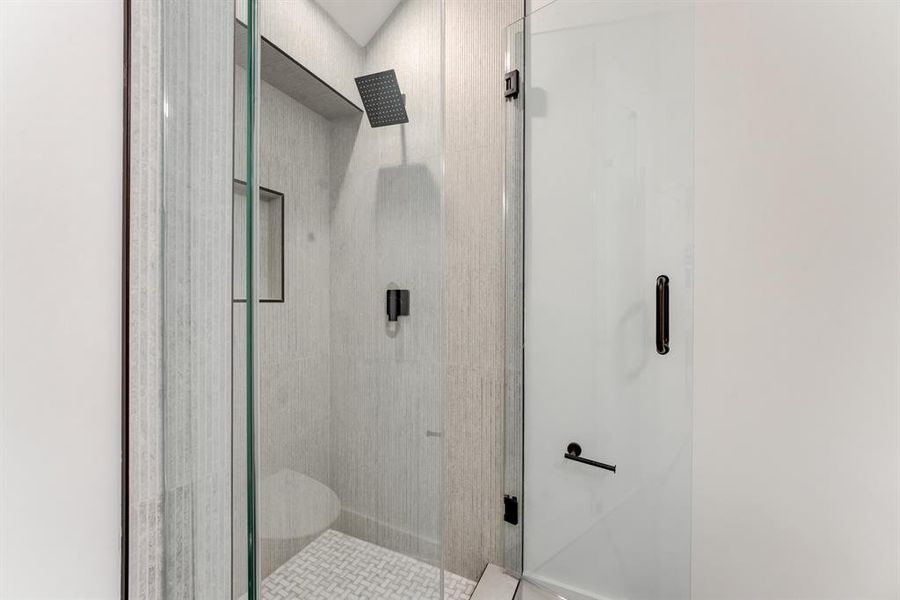 Frameless shower with black hardware accents and neutral toned tile.