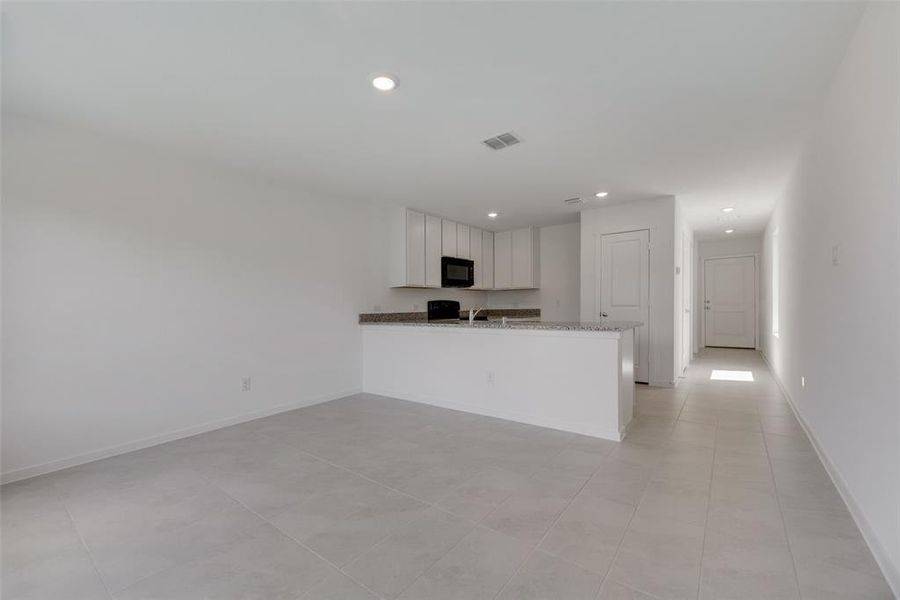 Kitchen featuring kitchen peninsula, light tile patterned flooring, black appliances, and white cabinets