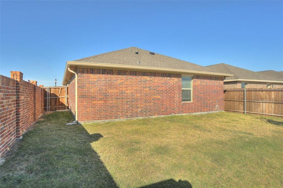 Back of house with a fenced backyard, brick siding, and a shingled roof