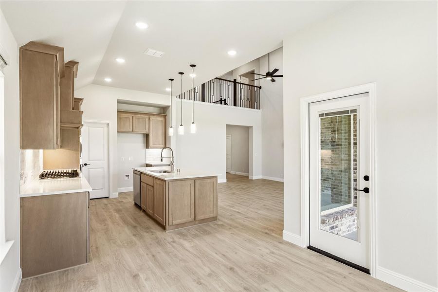 Open kitchen with center island, tan wood cabinets, pendant lights, and high ceilings with upstairs loft railing visible