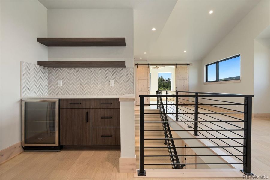 Dry bar in upper loft with beverage fridge and floating shelves
