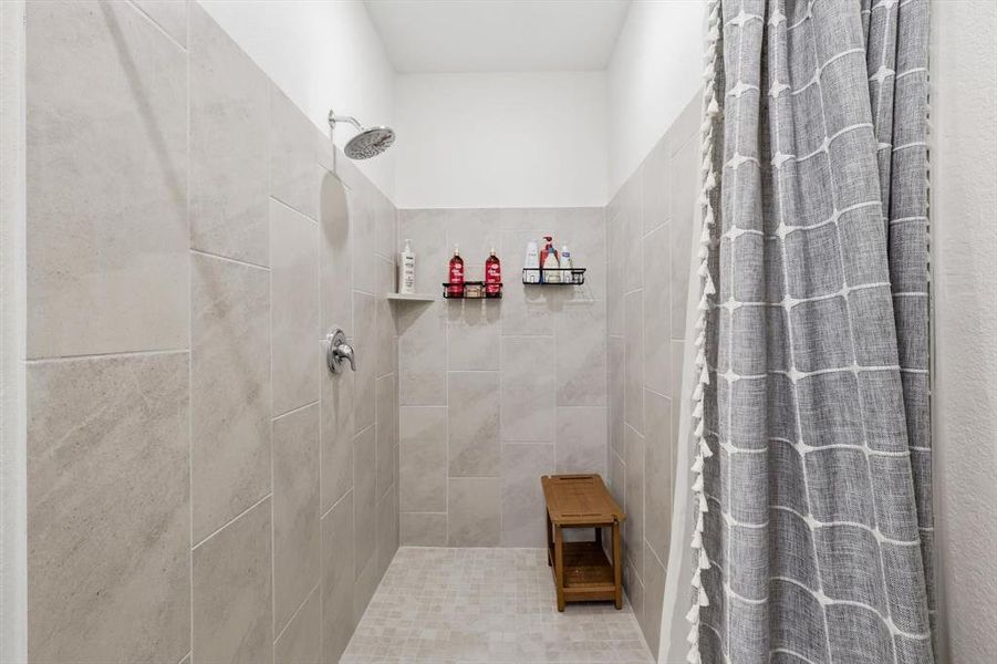 Walk-in shower featuring large format wall tiles, a mosaic tile floor, and a rainfall showerhead Walk-in shower featuring large format wall tiles, a mosaic tile floor, and a rainfall showerhead