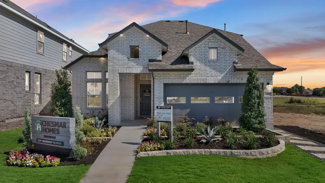 A striking modern home with brick siding and well-maintained landscaping at dusk. A striking modern home with brick siding and well-maintained landscaping at dusk.