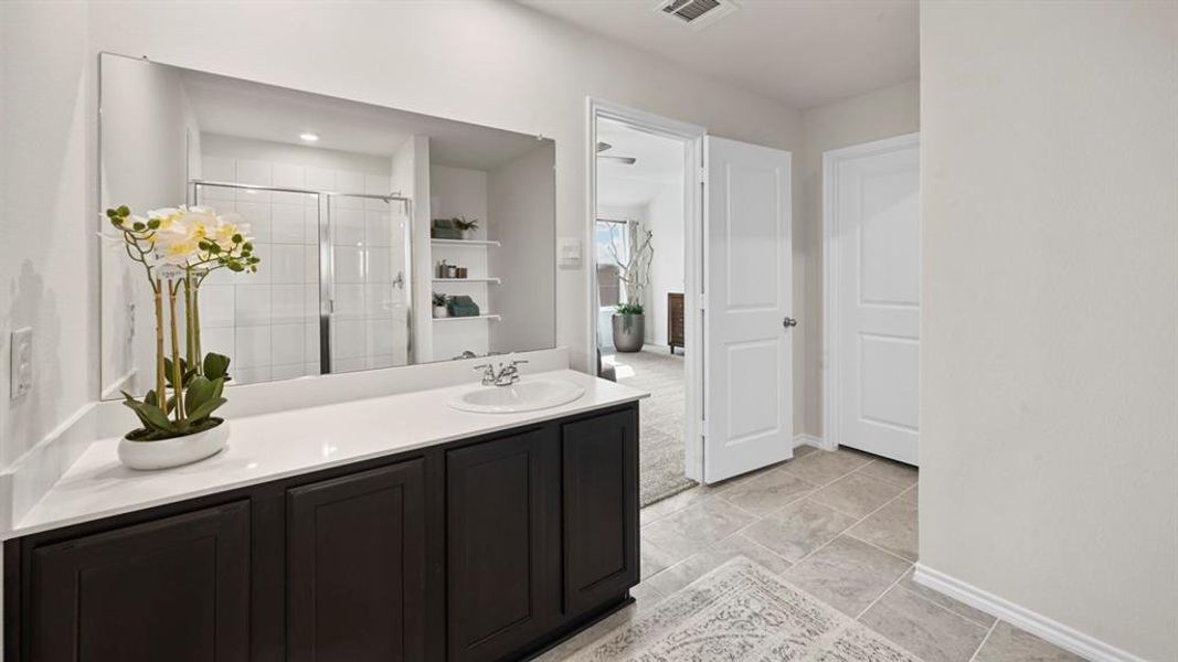 Bathroom featuring a dark wood vanity with a white countertop and an integrated sink, a large mirror, and tiled flooring