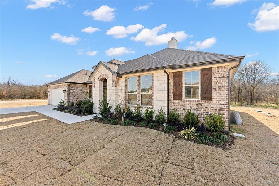 French country home featuring driveway, roof with shingles, a chimney, stone siding, and brick siding