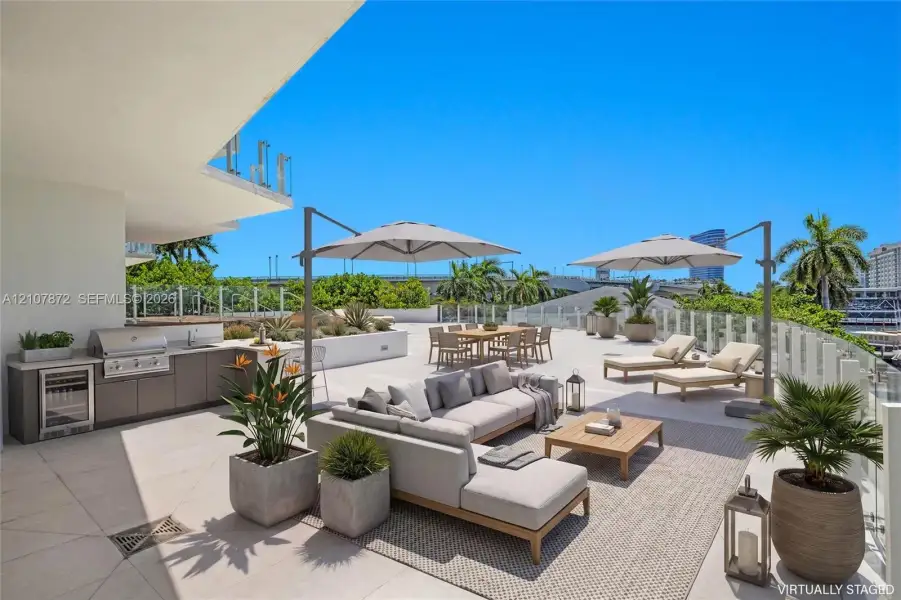 Expansive outdoor terrace featuring stone-tiled flooring, a built-in outdoor kitchen with stainless steel appliances, a bar refrigerator, and glass panel railing Expansive outdoor terrace featuring stone-tiled flooring, a built-in outdoor kitchen with stainless steel appliances, a bar refrigerator, and glass panel railing