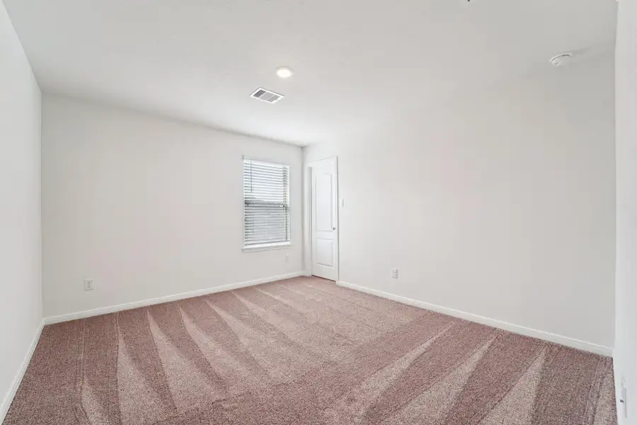 This secondary bedroom offers comfort and style with plush carpeting, neutral paint tones, recessed lighting, a large window with blinds, and a walk-in closet.