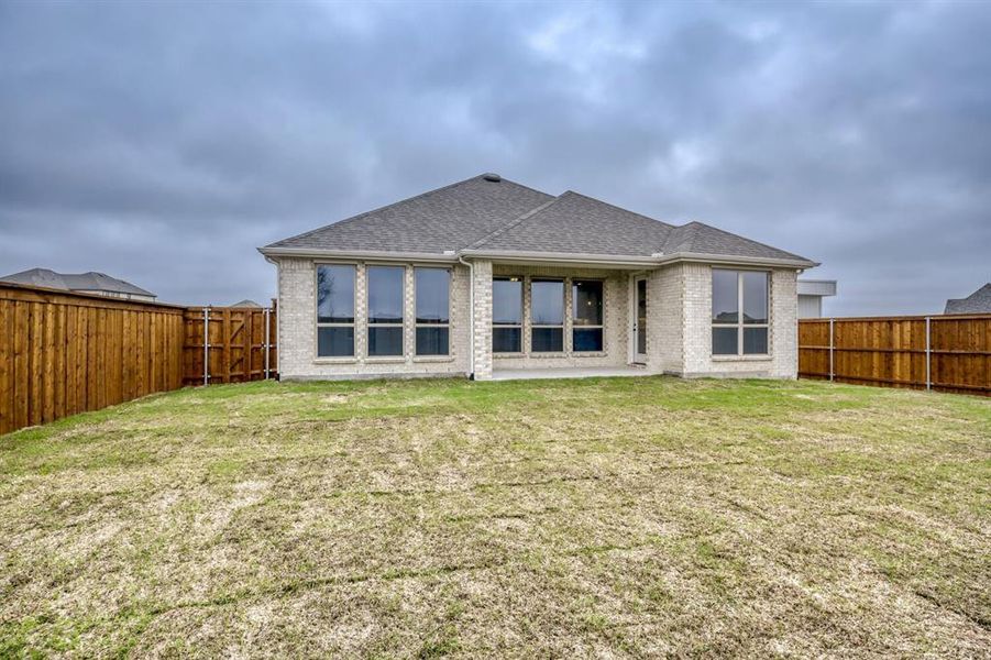 Rear view of house with roof with shingles, brick siding, a fenced backyard, and a patio
