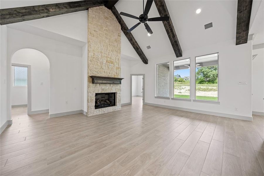 Unfurnished living room with a ceiling fan, beamed ceiling, high vaulted ceiling, arched walkways, and a stone fireplace Unfurnished living room with a ceiling fan, beamed ceiling, high vaulted ceiling, arched walkways, and a stone fireplace