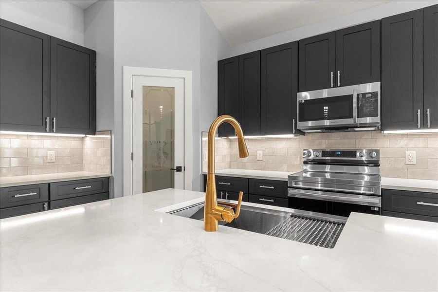 Kitchen with appliances with stainless steel finishes, dark cabinets, light stone counters, and backsplash Kitchen with appliances with stainless steel finishes, dark cabinets, light stone counters, and backsplash