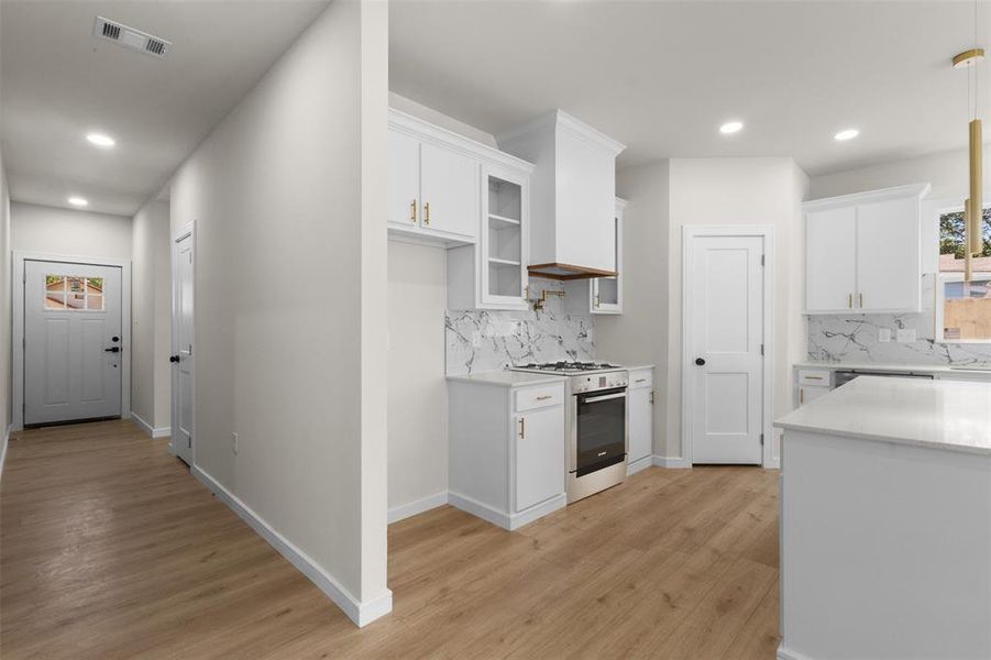 Contemporary kitchen featuring white cabinetry, a built-in stainless steel range, quartz countertops, a marble-look backsplash, and wood-finish flooring