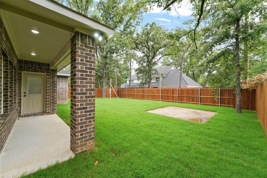 Expansive rear yard featuring a privacy fence, mature trees, and a concrete patio slab Expansive rear yard featuring a privacy fence, mature trees, and a concrete patio slab