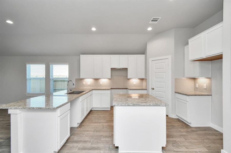 Another view of the culinary haven, featuring granite countertops, a tile backsplash, stainless steel appliances, 42” upper cabinets, and undercabinet lighting. Sample photo of completed home with similar floor plan. As-built interior colors and selections may vary.