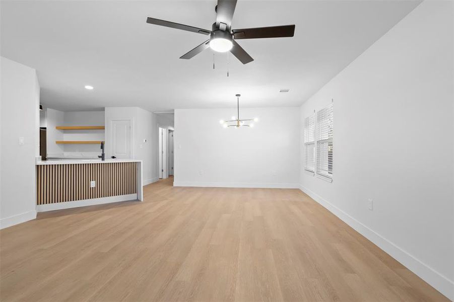 Unfurnished living room with ceiling fan with notable chandelier and light hardwood / wood-style floors