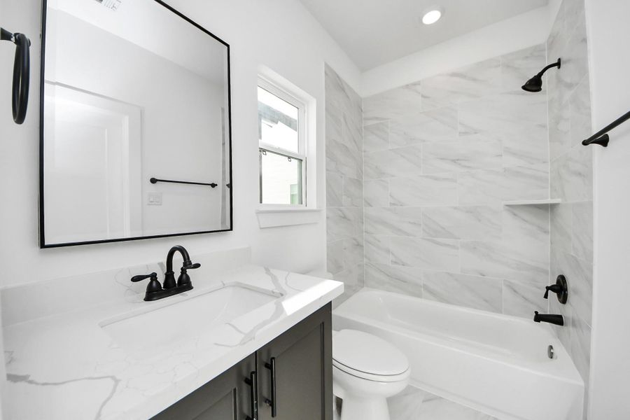 This bathroom features a modern design with a white and gray color scheme. It includes a sleek vanity with a marble countertop, a large mirror, and matte black fixtures. The bathtub is surrounded by elegant tile work, creating a fresh and clean look.