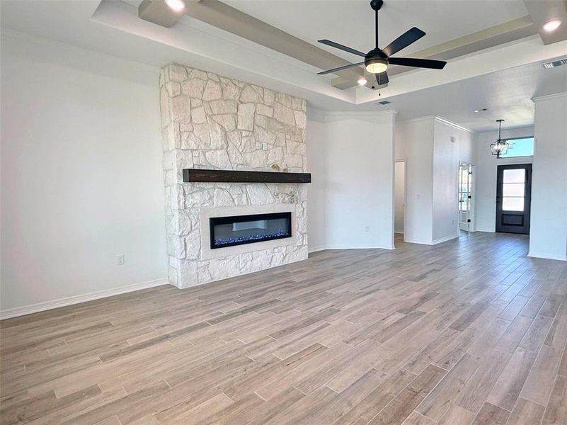 Unfurnished living room with light wood-style floors, a fireplace, a ceiling fan, and a raised ceiling