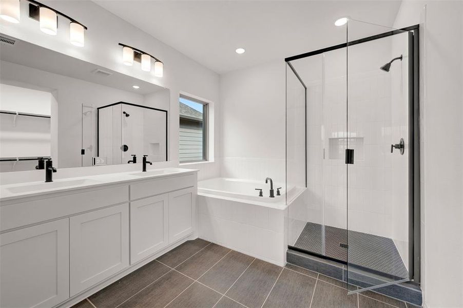 Full bathroom with a bath, a shower stall, double vanity, a spacious closet, and dark tile patterned floors