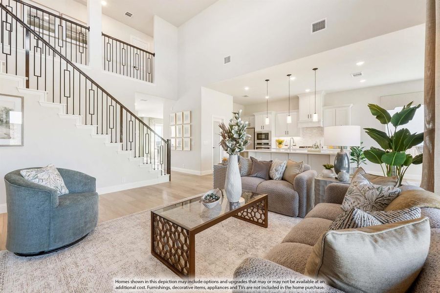 Open-concept living room with two-story ceiling, staircase, and kitchen visible in background