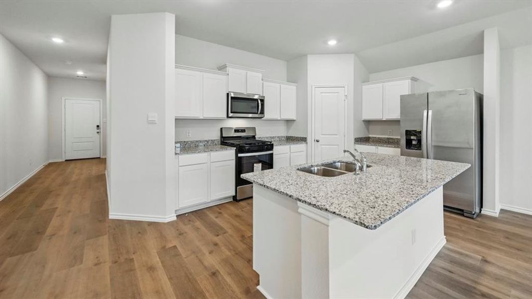 Kitchen featuring a central island with a double basin sink, light-toned countertops, white cabinetry, stainless steel appliances, and wood-finish flooring
