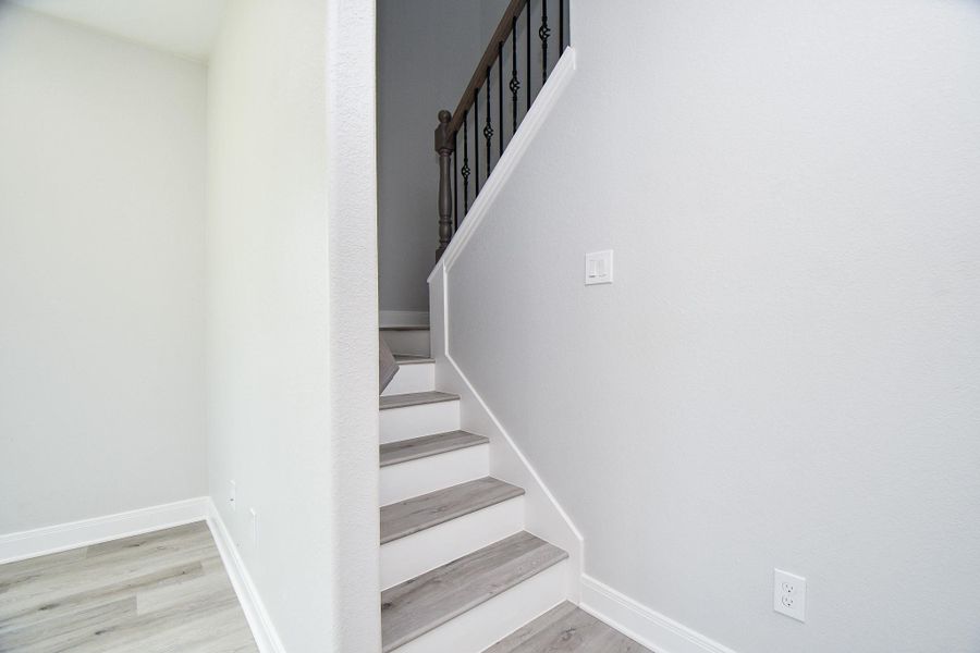This photo features a modern staircase with light wood steps and white walls, complemented by a dark wooden handrail with decorative iron balusters. The space is bright, with ample natural light and a clean, minimalist design.
