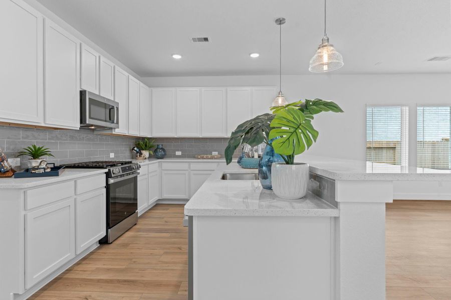 Contemporary kitchen design includes stainless steel appliances, quartz countertops, ceramic tile backsplash, and abundant white cabinetry—ideal for the home chef. **Image Representative of Plan Only and May Vary as Built**.