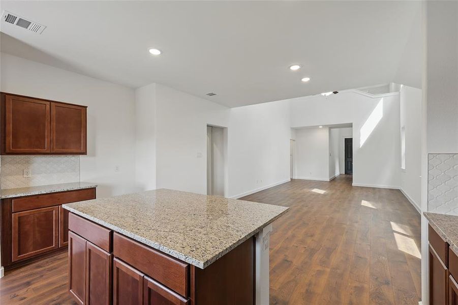Kitchen featuring dark wood-type flooring, light stone countertops, decorative backsplash, a kitchen island, and recessed lighting