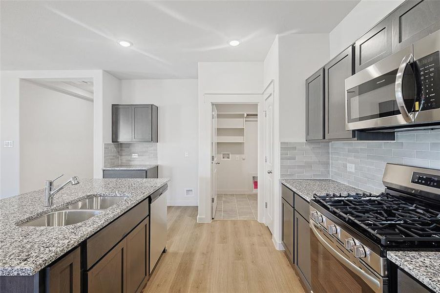 Kitchen featuring light stone countertops, sink, stainless steel appliances, backsplash, and light wood-type flooring