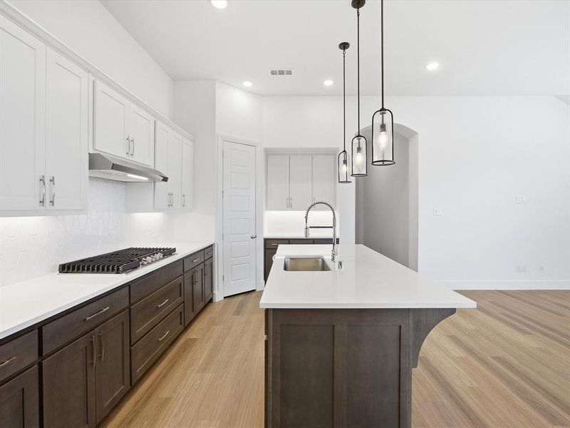 Kitchen featuring dual tone cabinetry, decorative light fixtures, light wood finished floors, a kitchen island with sink, and stainless steel gas stovetop
