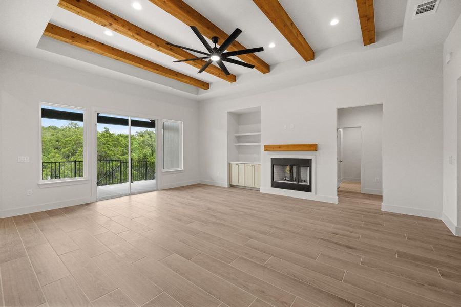 A spacious living room features exposed wooden beams, a modern fireplace, and floor-to-ceiling glass overlooking green vistas.