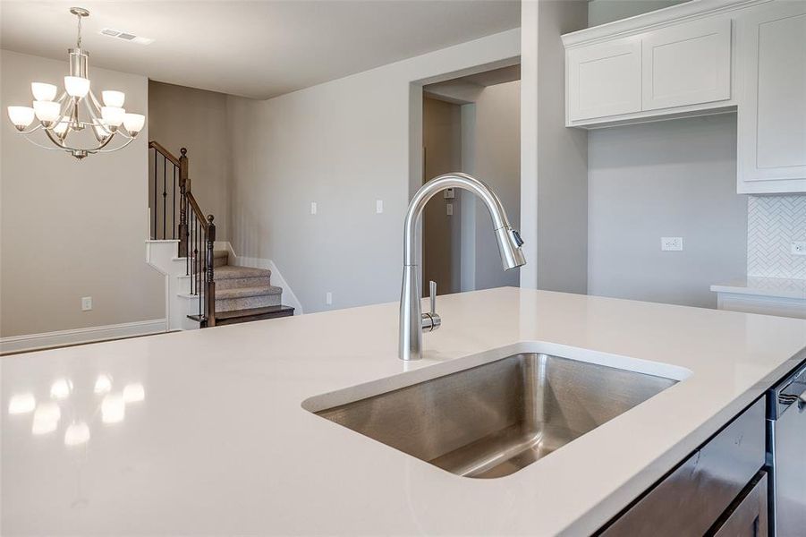 Kitchen featuring sink, white cabinetry, backsplash, a chandelier, and pendant lighting Kitchen featuring sink, white cabinetry, backsplash, a chandelier, and pendant lighting