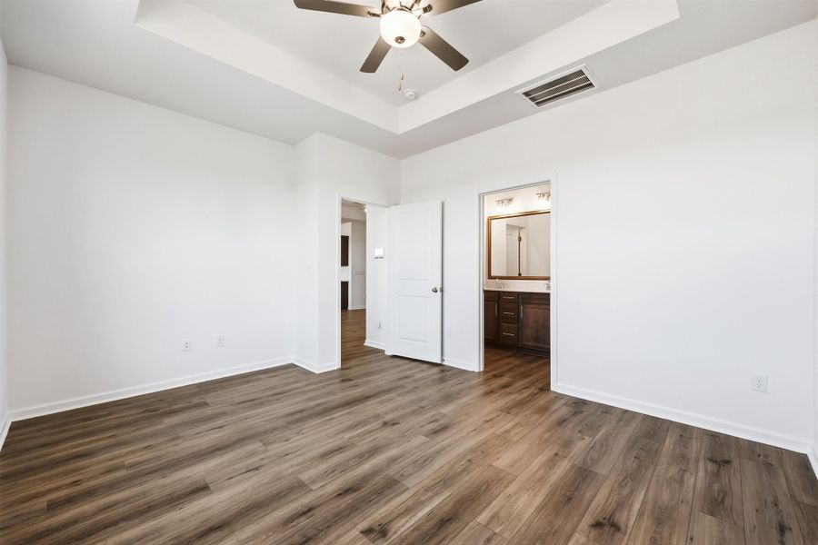 Unfurnished bedroom featuring a tray ceiling, dark wood-style flooring, a ceiling fan, and connected bathroom