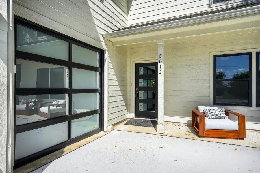 Modern facade with a sleek glass-paneled garage door and a welcoming entry. Modern facade with a sleek glass-paneled garage door and a welcoming entry.
