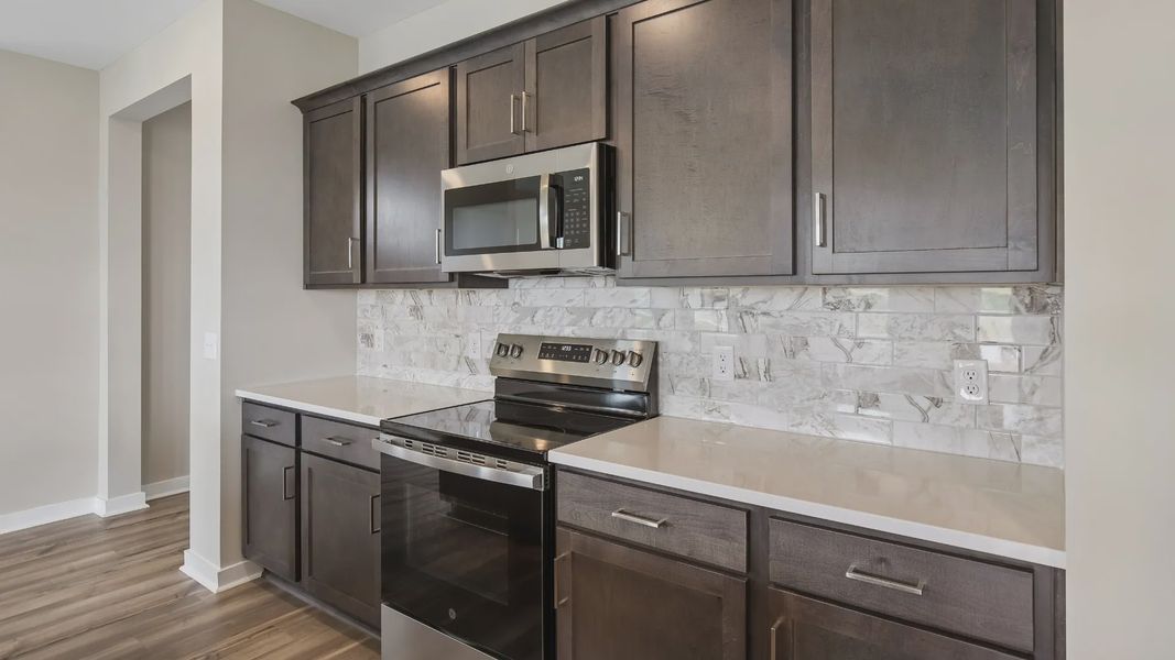 Kitchen with dark cabinetry, quartz countertops, stainless steel appliances, and tile backsplash Kitchen with dark cabinetry, quartz countertops, stainless steel appliances, and tile backsplash