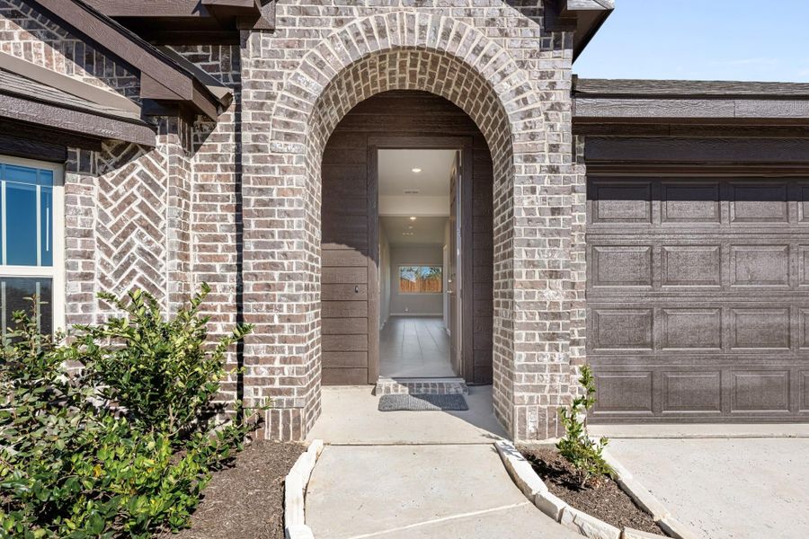 Home entrance with brick arched doorway, open front door, and attached two-car garage beside landscaped walkway