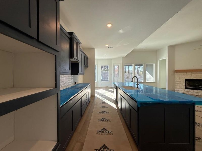 Kitchen with backsplash, dark cabinets, a center island with sink, wood finished floors, and open floor plan