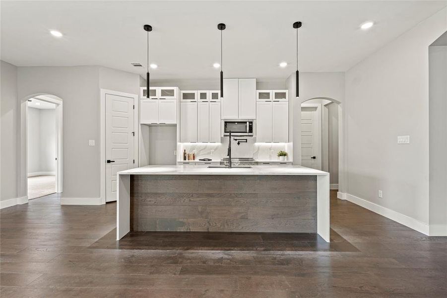 Kitchen featuring arched walkways, stainless steel microwave, dark wood finished floors, and recessed lighting